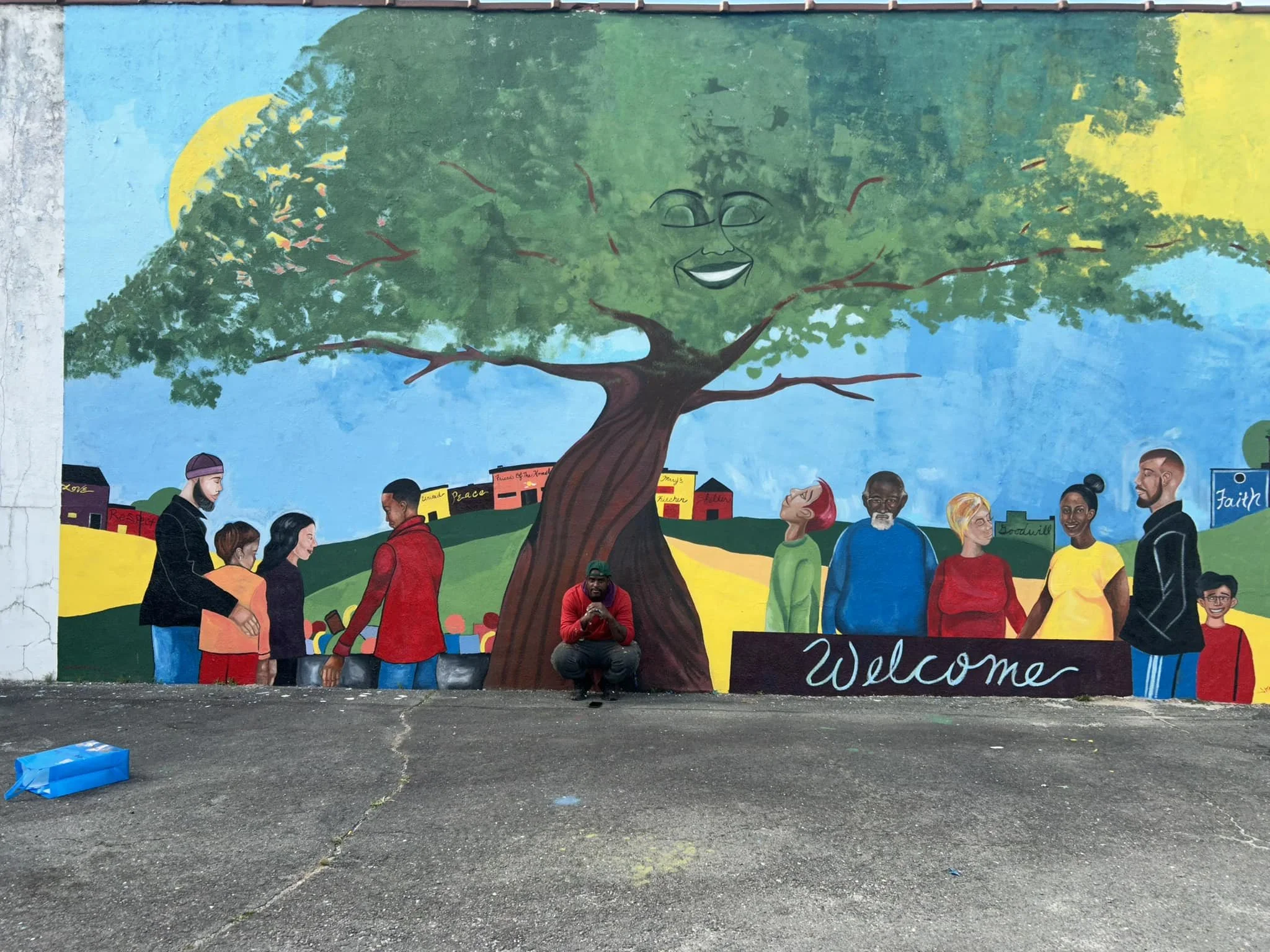 The shelter's colorful Welcome mural showing neighbors gathered beneath a large tree